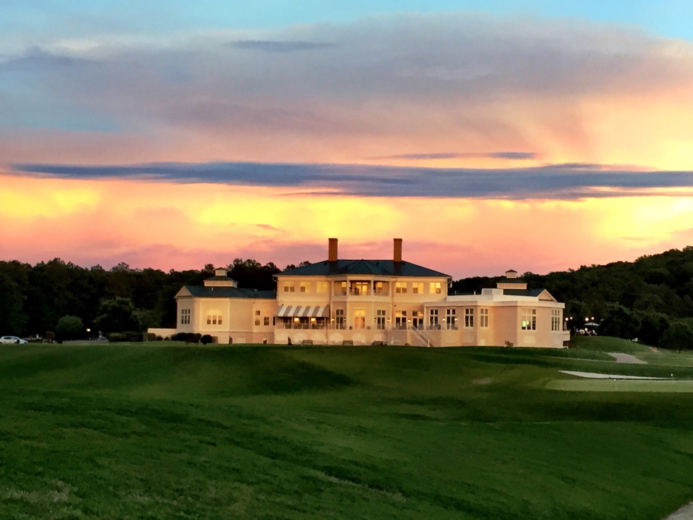 The Independence Golf Club clubhouse glowing at sunset above the eighteenth fairway.